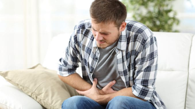 Man suffering stomach ache sitting on a couch in the living room at home