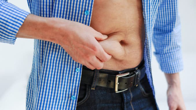 man wearing a blue and white checkered shirt is pinching his belly fat with his right hand