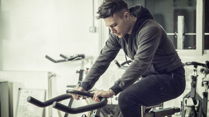 Attractive young man exercise in gym: spinning, exercising on stationary bike