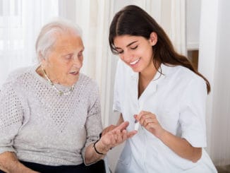 Happy Female Doctor Checking Blood Sugar Level Of Senior Patient With Glucometer In Clinic