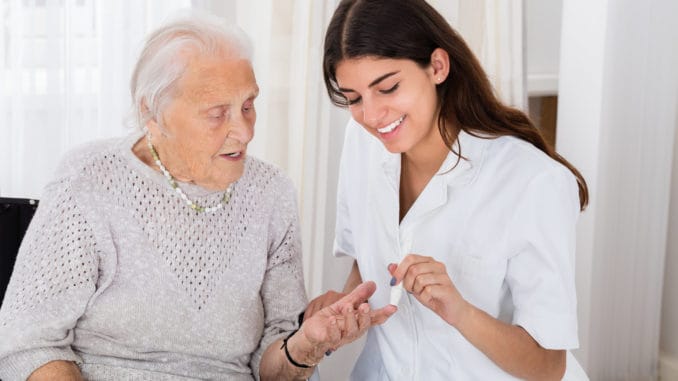 Happy Female Doctor Checking Blood Sugar Level Of Senior Patient With Glucometer In Clinic