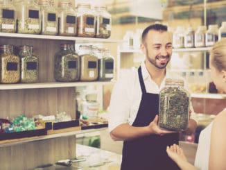 Man seller holding glass can with dried herbs in organic shop