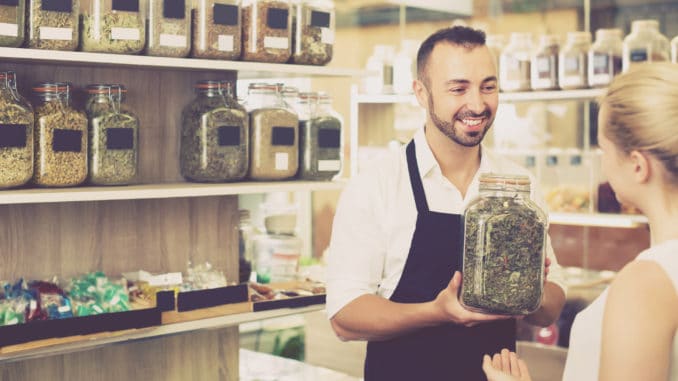 Man seller holding glass can with dried herbs in organic shop