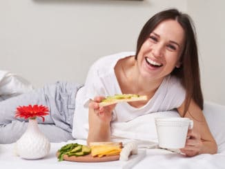 Mid shot of beautiful smiling girl eating sandwich with avocado and drinking aromatic tea