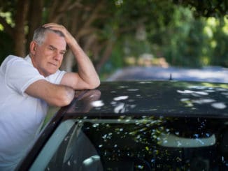 Tensed senior man with head in hand leaning on car