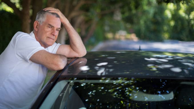 Tensed senior man with head in hand leaning on car