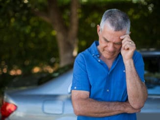 Tensed senior man standing by car against trees