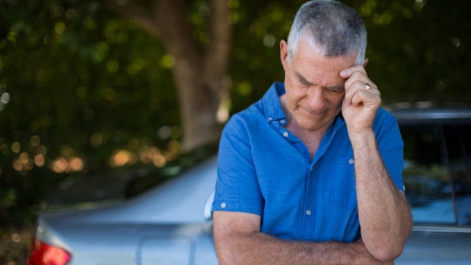 Tensed senior man standing by car against trees