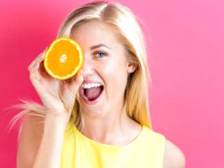 Happy young woman holding oranges halves on a pink background