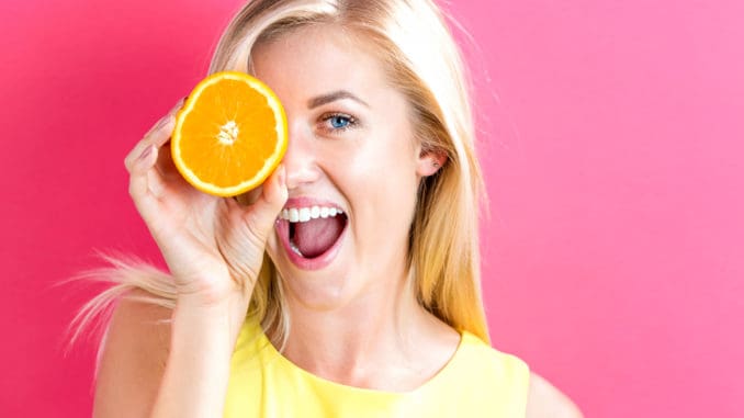 Happy young woman holding oranges halves on a pink background