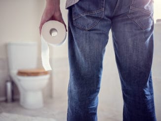 Man holding toilet tissue roll in bathroom looking at loo