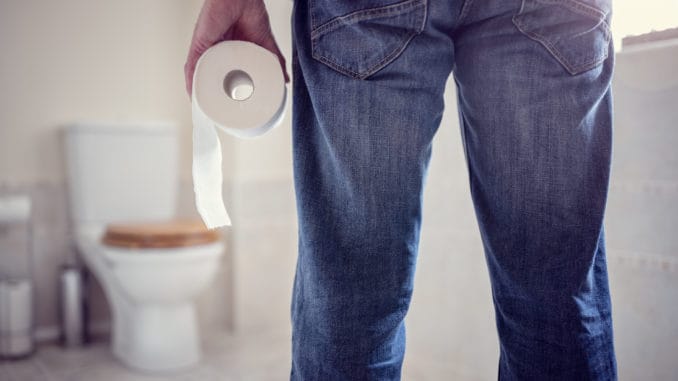 Man holding toilet paper roll in bathroom Man holding toilet tissue roll in bathroom looking at loo