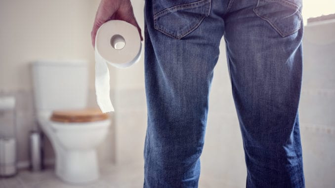 Man holding toilet tissue roll in bathroom looking at loo