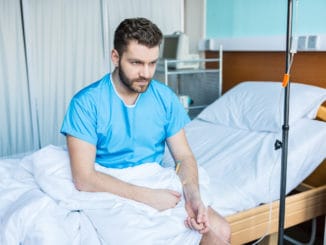 Sick bearded man sitting on hospital bed with drop counter