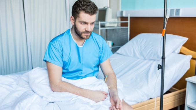 Sick bearded man sitting on hospital bed with drop counter