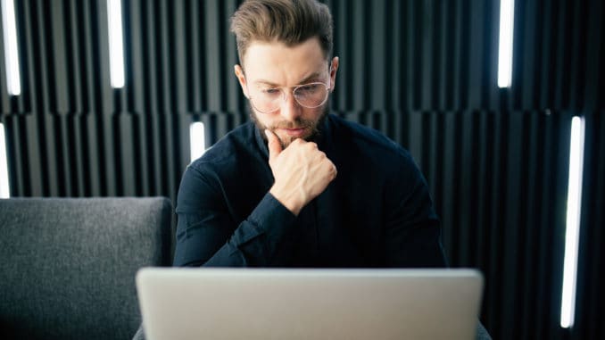 Shot of young man sitting at table looking away and thinking. Thoughtful businessman sitting office.