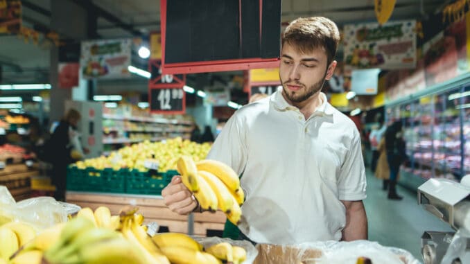 A handsome bearded man buys bananas in a supermarket