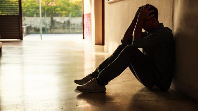 Emotional moment: man sitting holding head in hands, stressed sad young male having mental problems