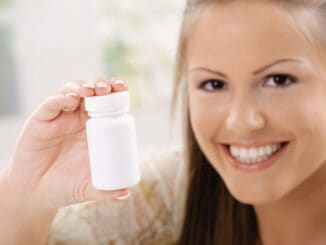 Beautiful young woman showing white pill bottle, copy space.