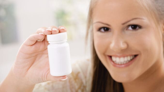 Beautiful young woman showing white pill bottle, copy space.