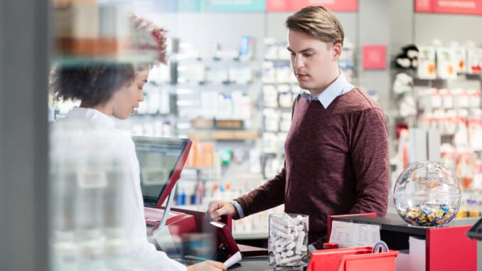 Portrait of a handsome young men smiling while buying an useful pharmaceutical product in a modern drugstore with various medicines and helpful personnel