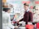 Portrait of a handsome young men smiling while buying an useful pharmaceutical product in a modern drugstore with various medicines and helpful personnel