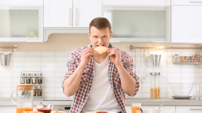 Young man eating tasty toasted bread at table in kitchen