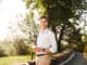 Happy young man in shirt walking at the city park with cup of coffee