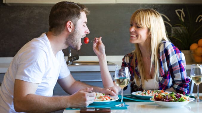 Shot of happy young couple enjoying lunch while women is feeding her boyfriend in the kitchen at home.
