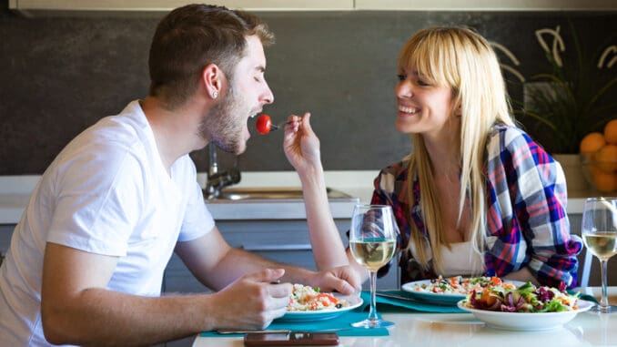 dreamstime_s_124072828 Shot of happy young couple enjoying lunch while women is feeding her boyfriend in the kitchen at home.