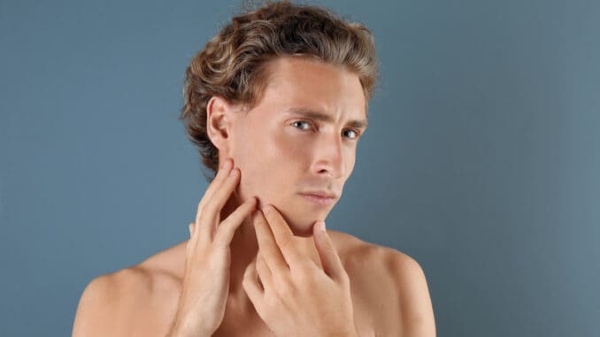 Young man touching his soft skin after shaving on gray background