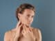 Young man touching his soft skin after shaving on gray background