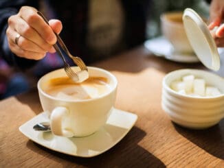 Man`s hand adding cube of white sugar to his coffee or cuppuchino