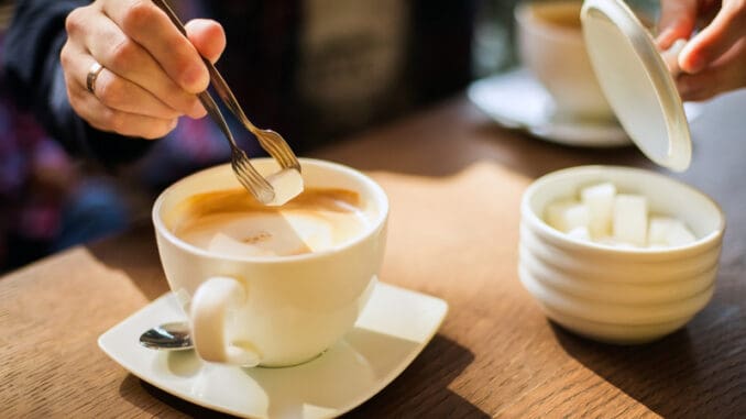 Man`s hand adding cube of white sugar to his coffee or cuppuchino