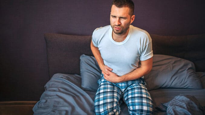 Young man stands on knees on bed and suffers from pain in appendix area.