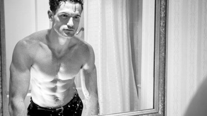 dreamstime_s_133862099 Attractive shirtless man with muscular body and sixpack abs looking at his reflection in bathroom mirror