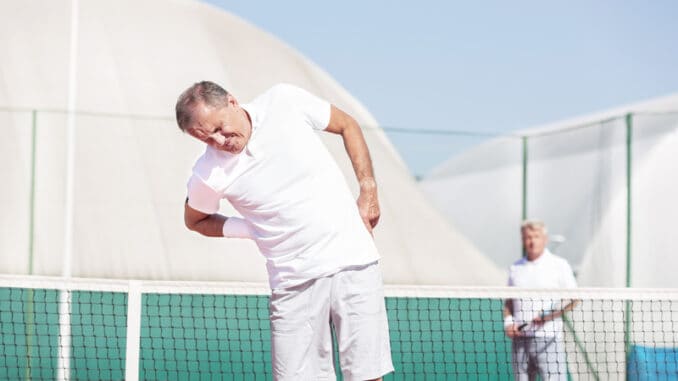 Senior men with backache while standing against friend during tennis match on sunny day