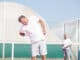 Senior men with backache while standing against friend during tennis match on sunny day