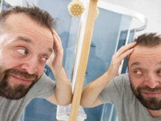 Happy man looking at his hair in bathroom mirror.