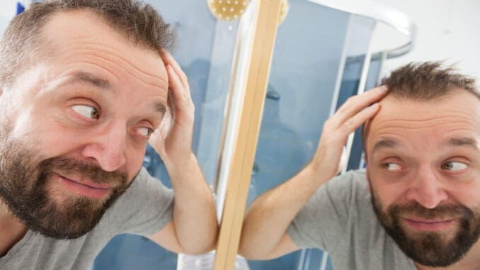 Happy man looking at his hair in bathroom mirror.