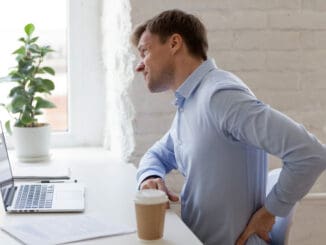 Unhealthy office worker sitting at desk opposite computer feels sudden sharp pain in lower back.