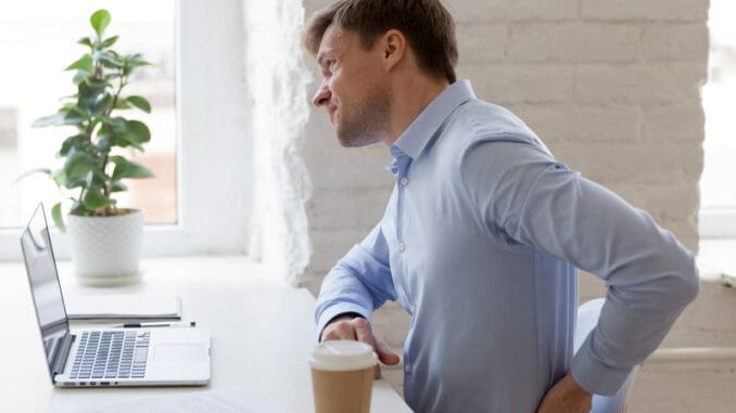 Unhealthy office worker sitting at desk opposite computer feels sudden sharp pain in lower back.