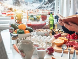 Man reading book with preparing food on dining table with snowing on village in wintertime