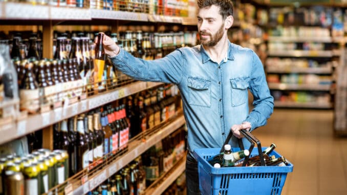 Man with thirst to alcohol taking beer from the shelves with strong drinks in the supermarket