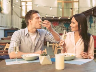Drinking sparkling wine. Light-haired boyfriend with stubble eating oyster directly from hard shell during lunch with his girl