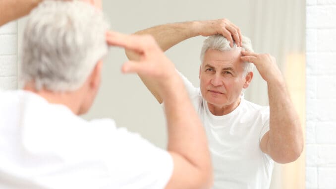 Senior man with hair loss problem looking in mirror indoors