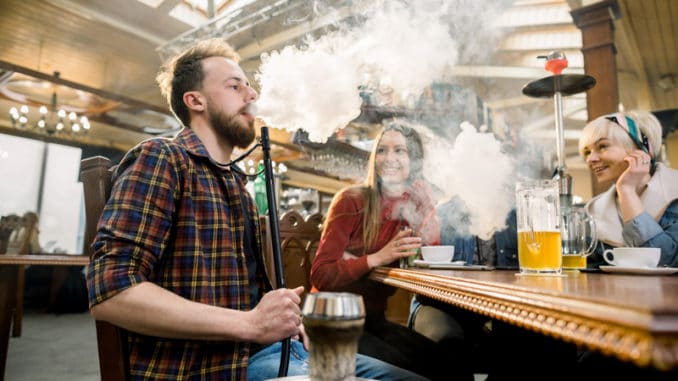 Close-up shot of a stylish bearded adult guy smoking hookah indoor of a cafe