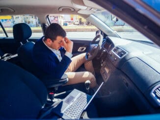 Reckless businessman driving in the city during the rush hour while typing on his laptop