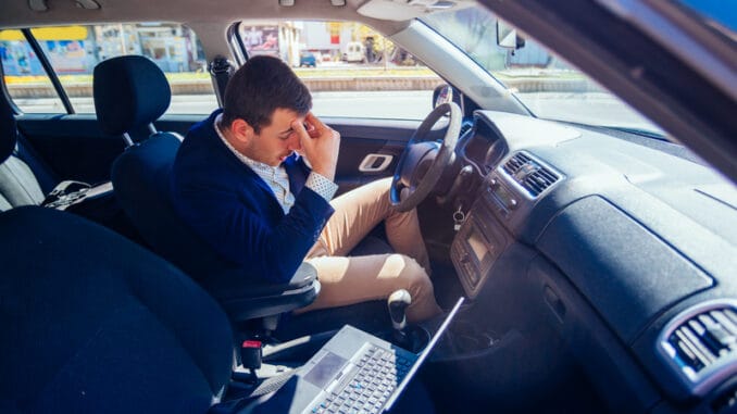 Reckless businessman driving in the city during the rush hour while typing on his laptop