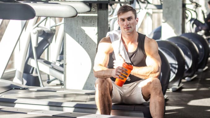 Portrait of confident athlete handsome masculine man sitting during treadmill exercise in gym